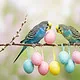 Zwei Wellensittiche sitzen zu Ostern auf einen Zweig mit bunten Ostereiern.
